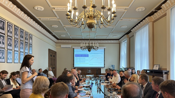 Telpa pilna ar cilvēkiem, kuri sēž ap galdu