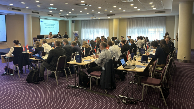 Telpā redzami daudz cilvēki, kuri sēž pie galdiem