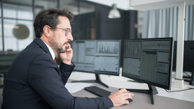 vīrietis pie datora ar mobilo telefonu