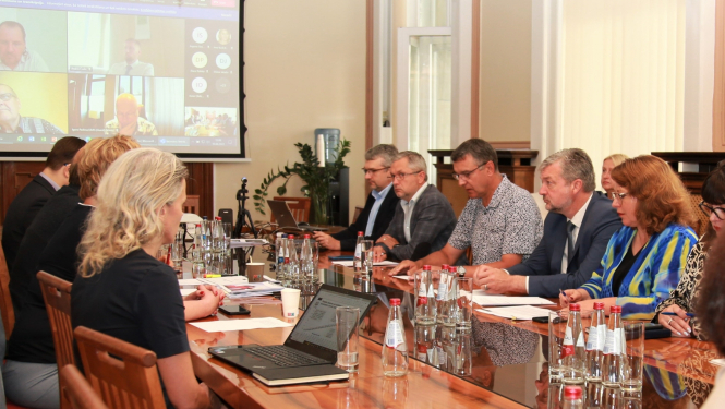 Sanāksme. Pie darba galda redzami vīrieši un sievietes diskutējam