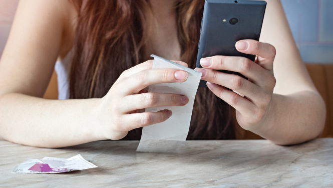 Sieviete tur rokās mobilo telefonu un veikala čeku