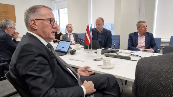 Konferenču zālē pie galda sēž vīrieši uzvalkos un diskutē