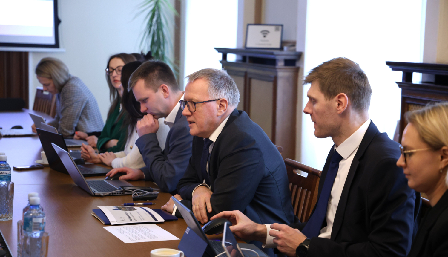 Pie galda sēž vīrieši un sievietes, kas savstarpēji diskutē