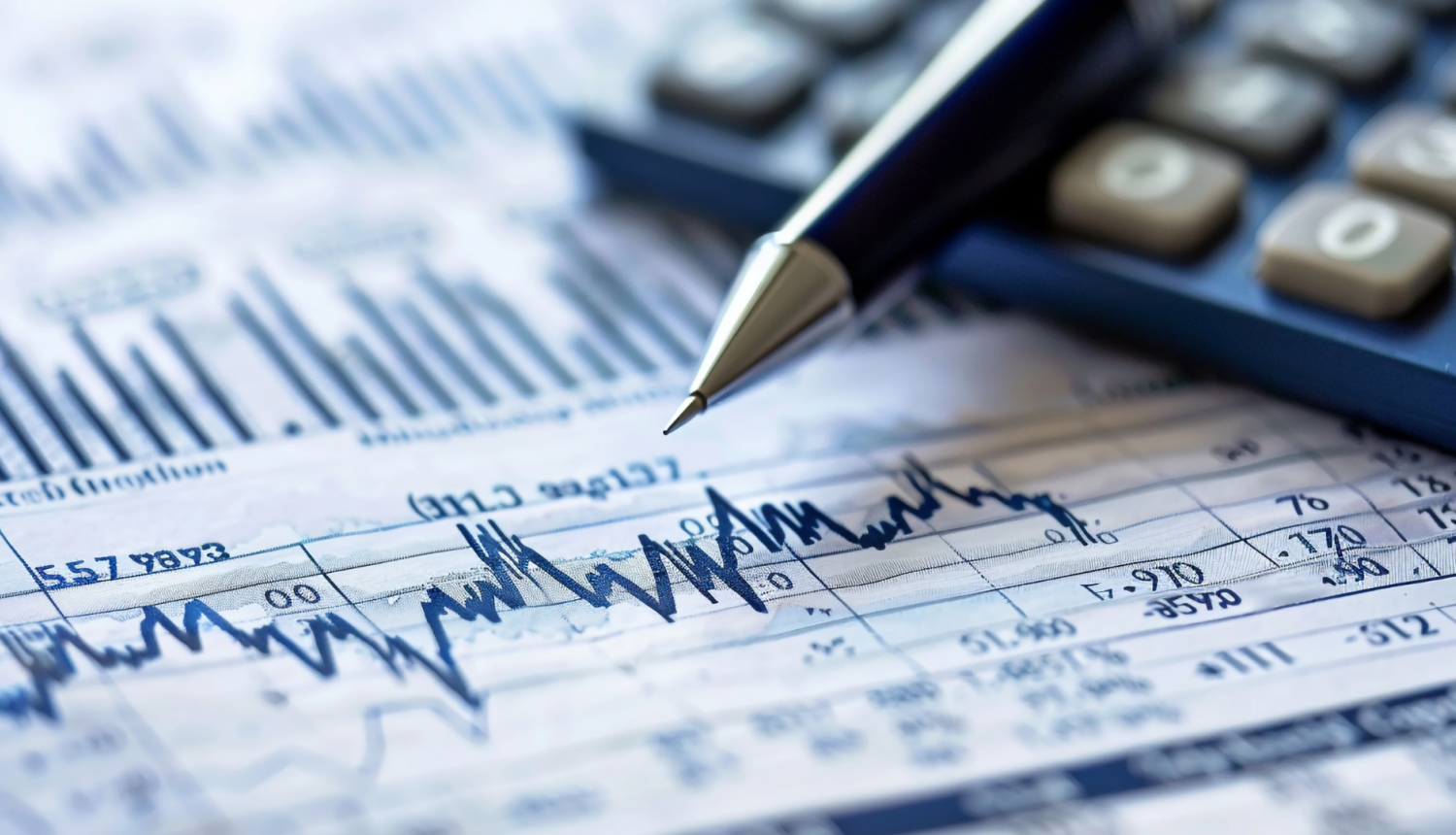 Attēlā tuvplānā redzami dokumenti ar dažādiem grafikiem un finanšu datiem un daļa no uz galda nolikta kalkulatora un pildspalva