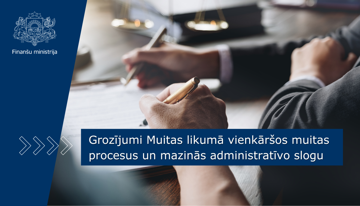 Attēlā redzama daļa no darba galda virsmas pie kā divi cilvēki paraksta dokumentu, uz attēla ir teksts