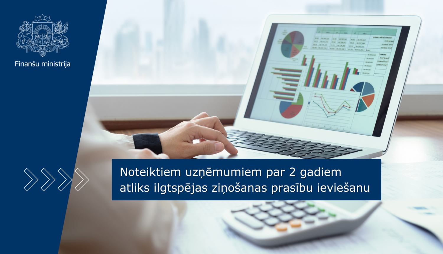 Attēlā uz galda redzams portatīvais dators, kura ekrānā redzami dažādi grafiki, vēl uz galda redzami dokumenti un kalkulators, kā arī cilvēka roka, kas strādā ar datoru