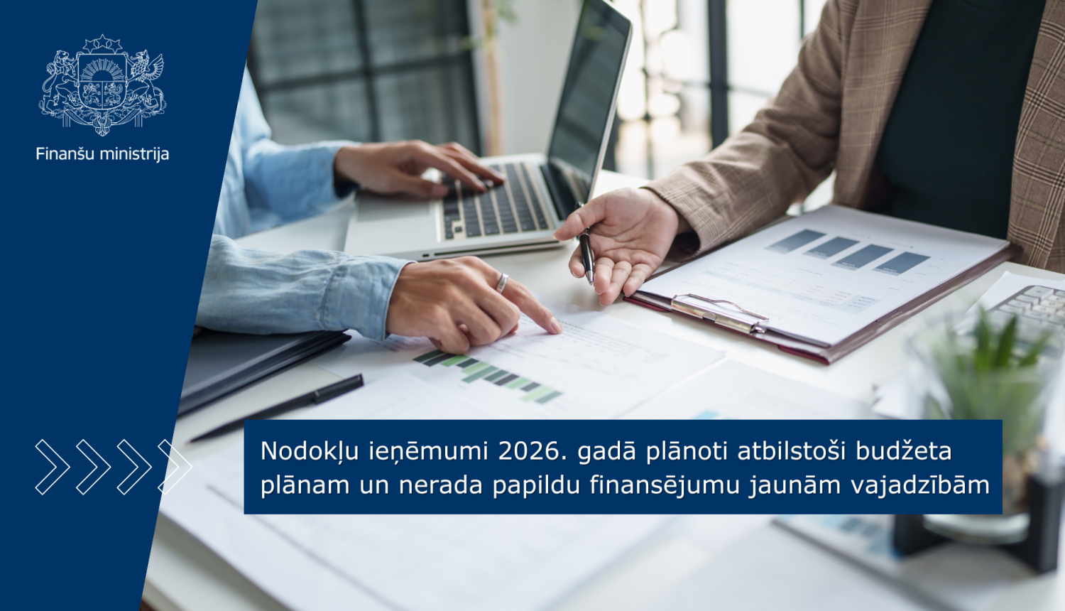 Pie darba gada sēž divi cilvēki un strādā ar dokumentiem un portatīvo datoru